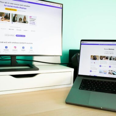 Office desk workspace with a laptop and a monitor displaying a social media wall solution.